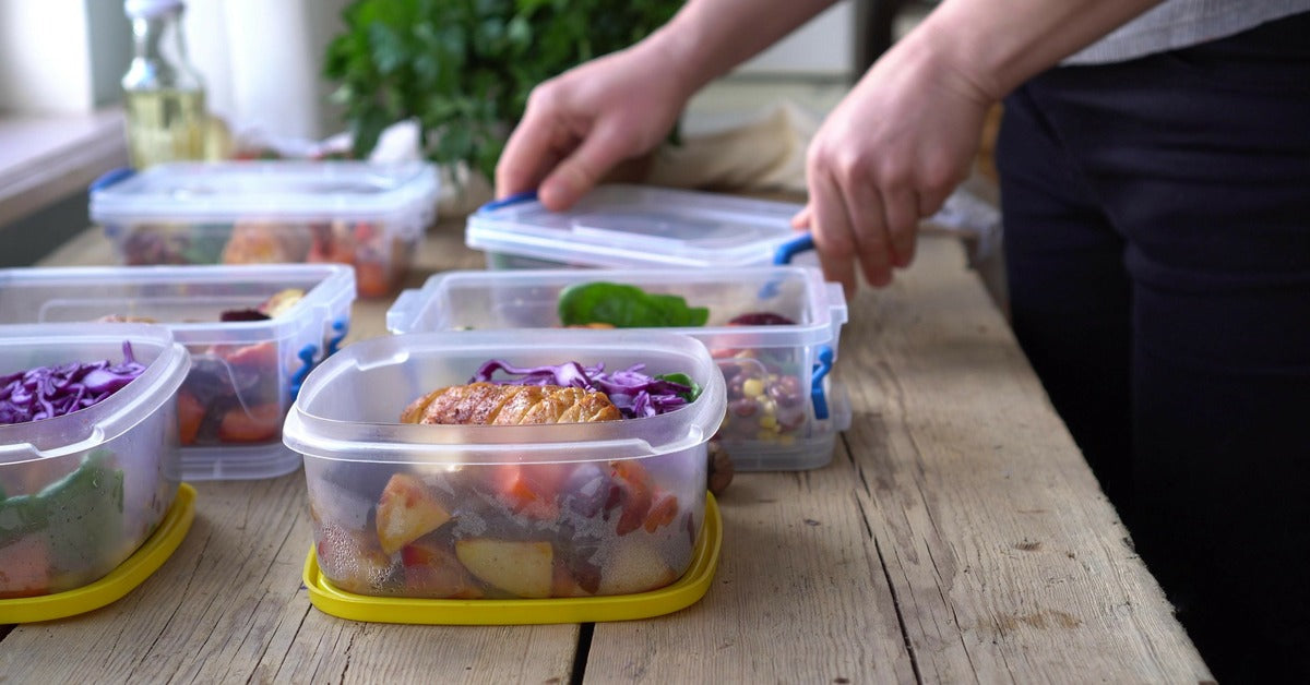 A person meal preps six containers with veggies and protein in their kitchen, organizing healthy meals.