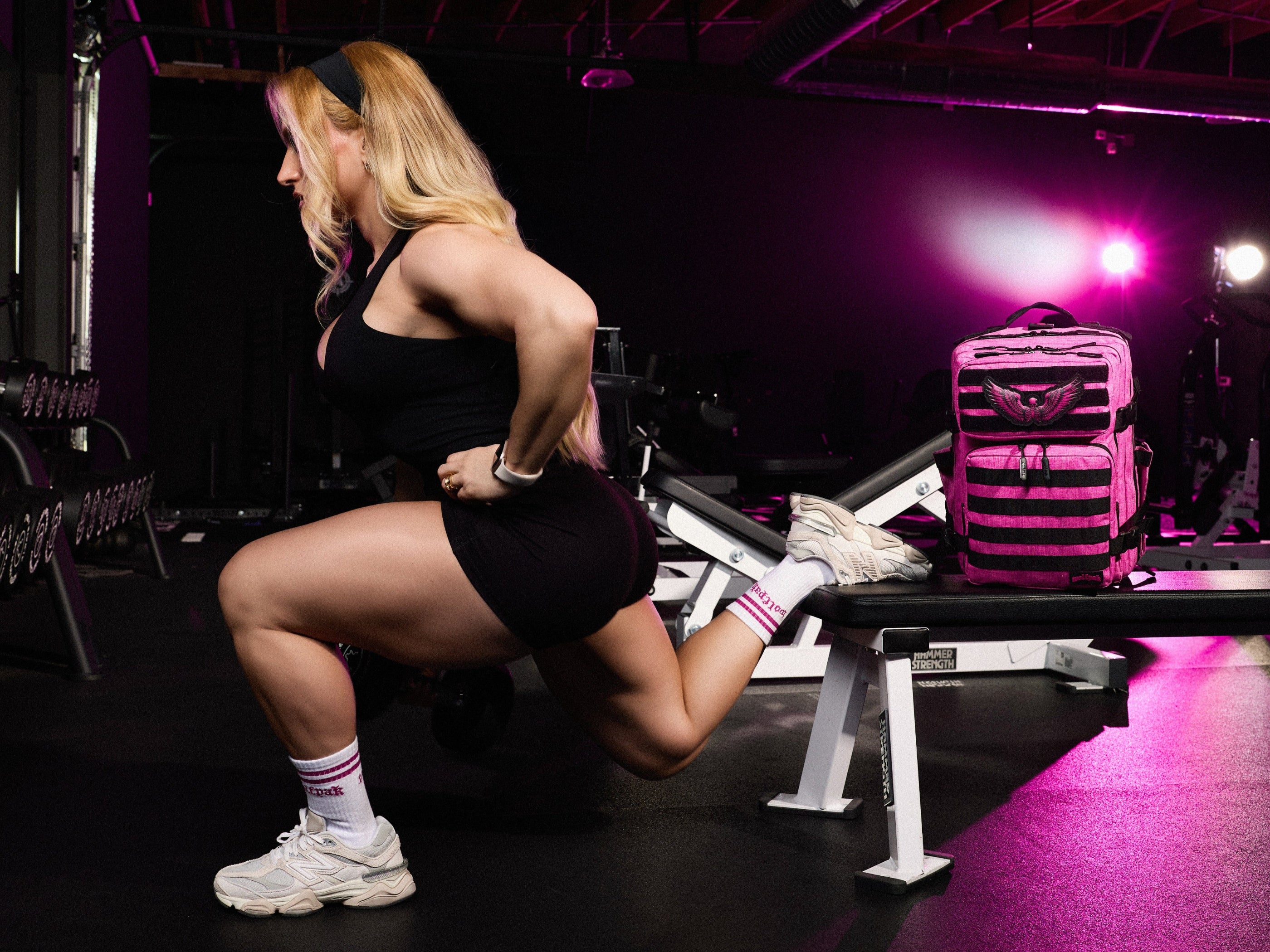 Woman exercising in a gym with a pink and black striped backpack on a bench.