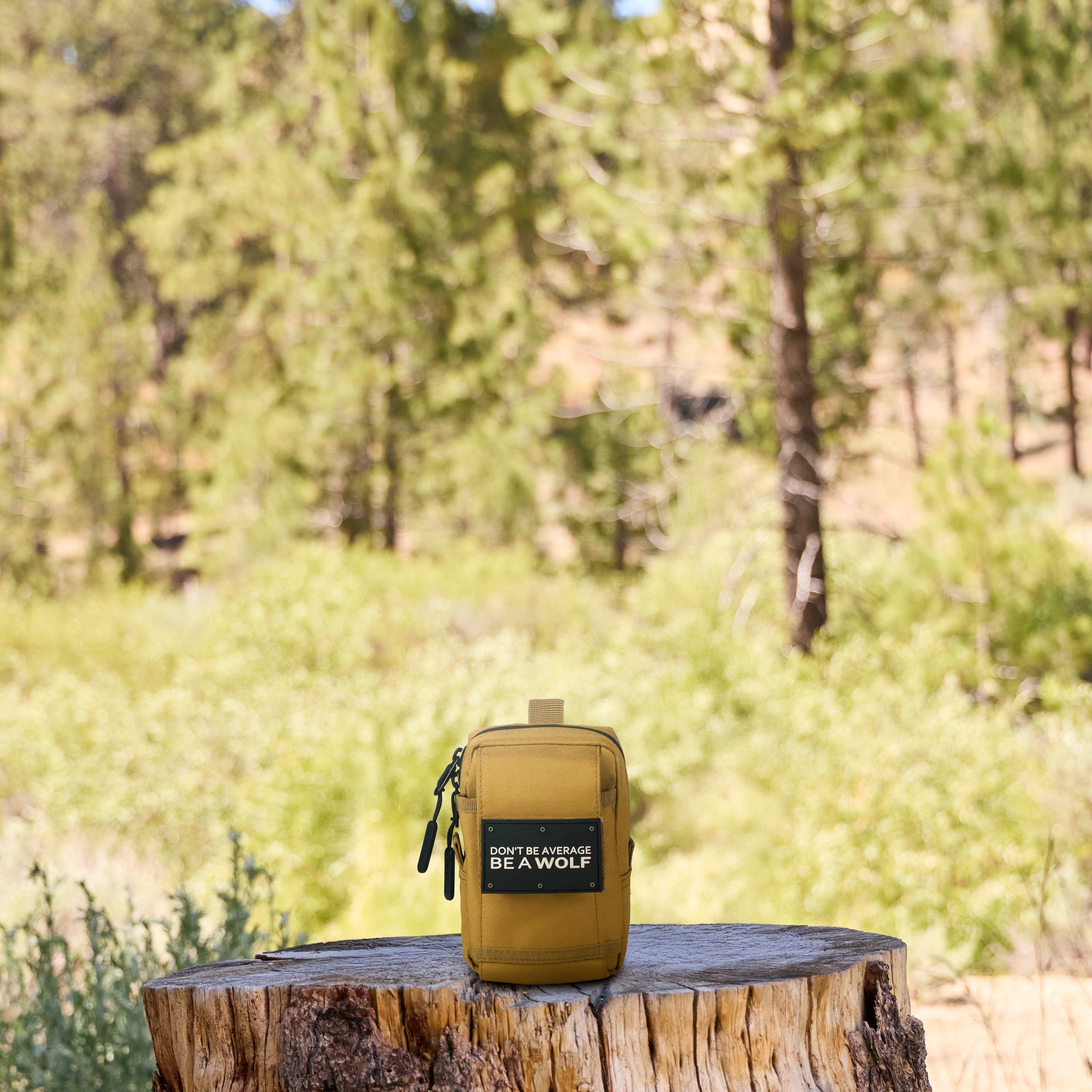Tan pouch with 'Don't Be Average, Be A Wolf' label on a wooden stump in a forest setting