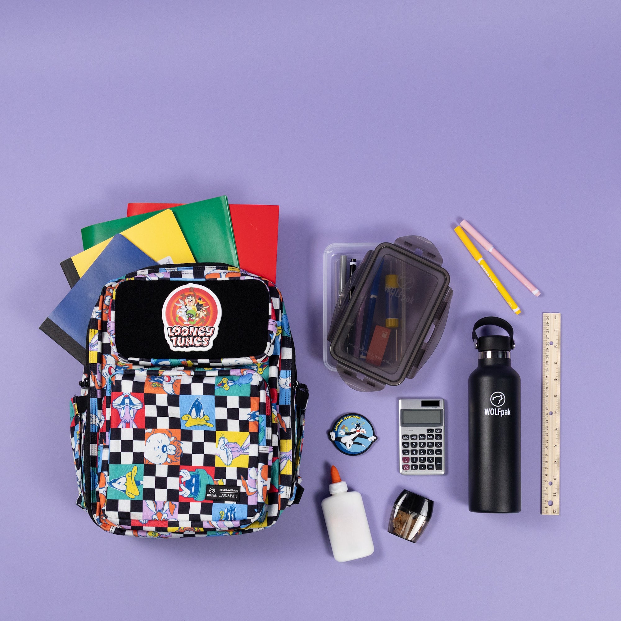 A colorful school backpack with a black-and-white checkered pattern and cartoon graphics, surrounded by school supplies on a solid lavender background. The backpack features a circular 'LOSENZY TUESDAY' patch on the front pocket.