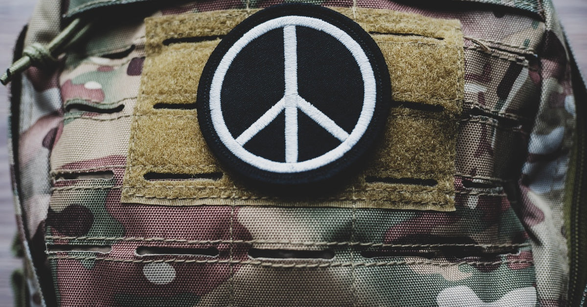  A military backpack has a black and white peace symbol morale patch attached to it.