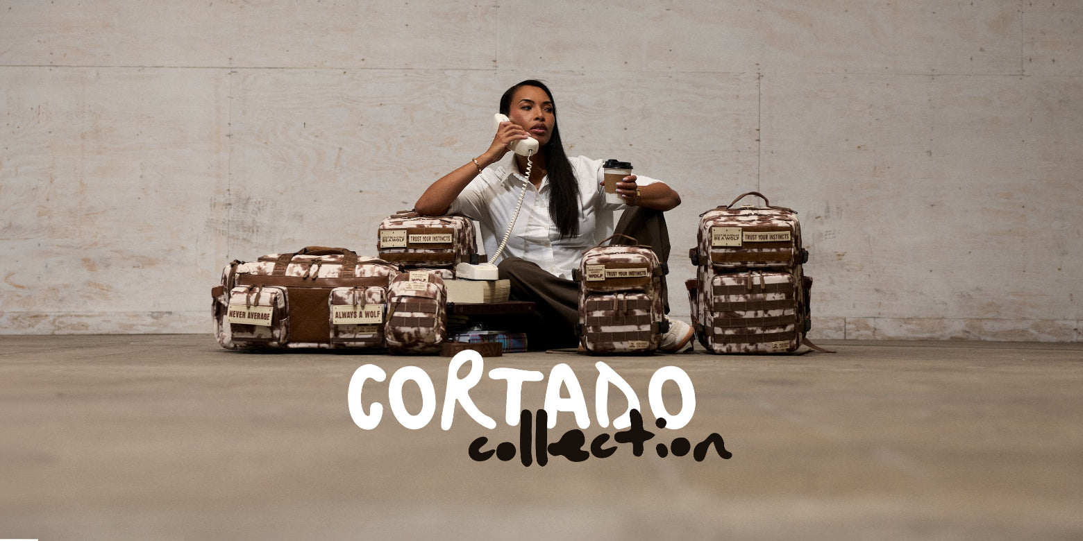 A person sits on the floor in front of a concrete wall, surrounded by multiple Cortado Collection backpacks and bags.