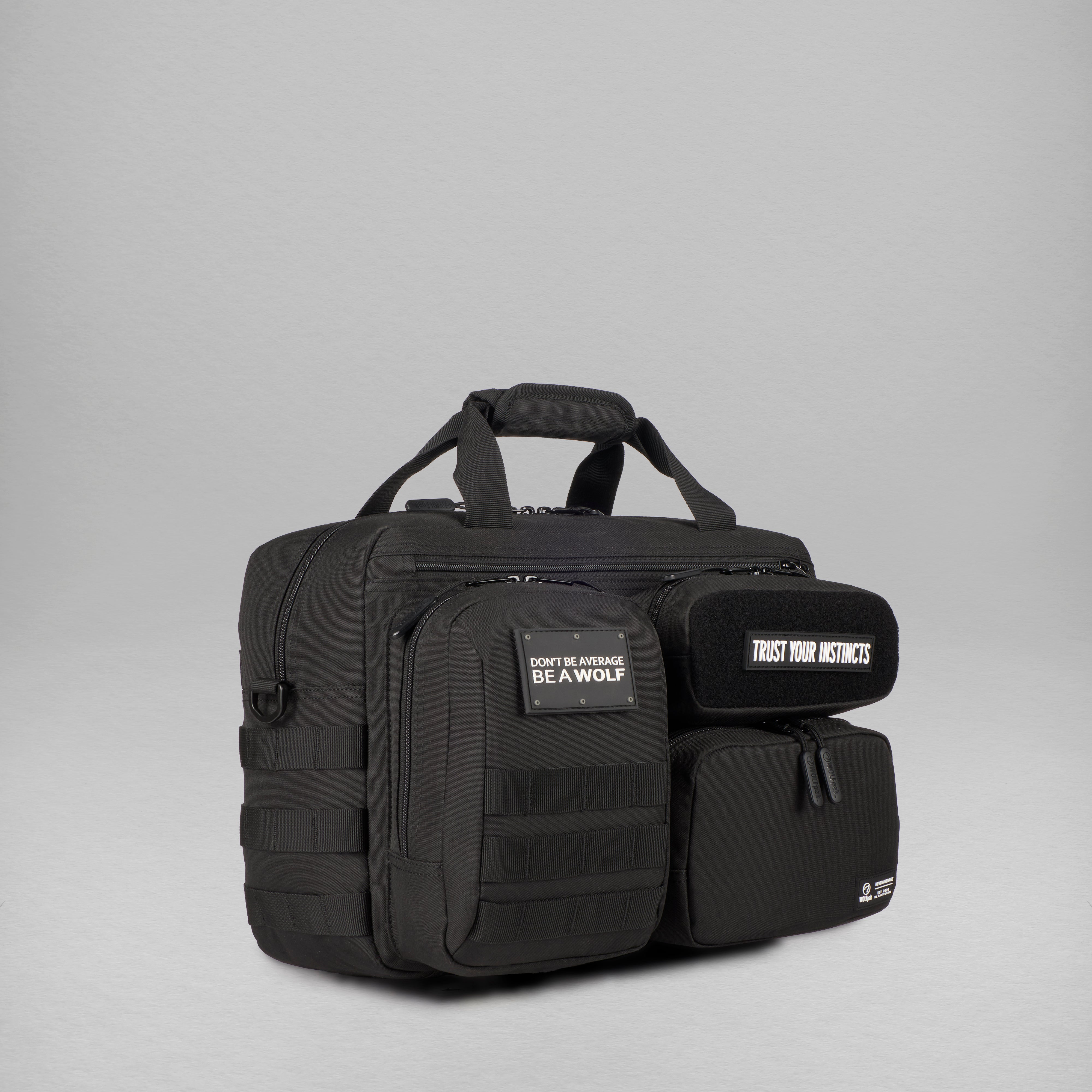 A black tactical briefcase with multiple zippered compartments, top handles, and branded patches, photographed on a neutral gray studio background.