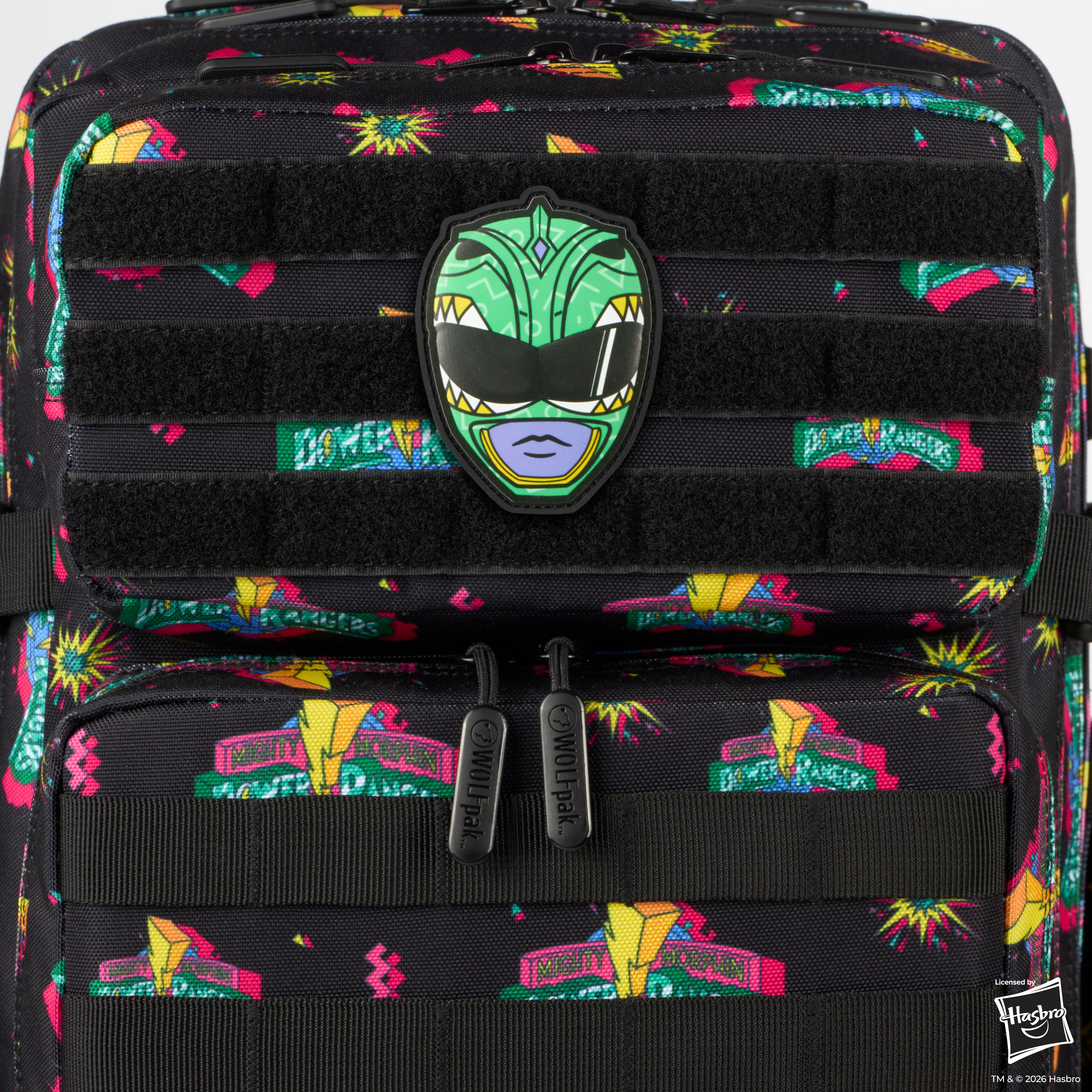 Close-up of a black tactical backpack featuring a colorful all-over print of Power Ranger logos and a green mask patch on the front.
