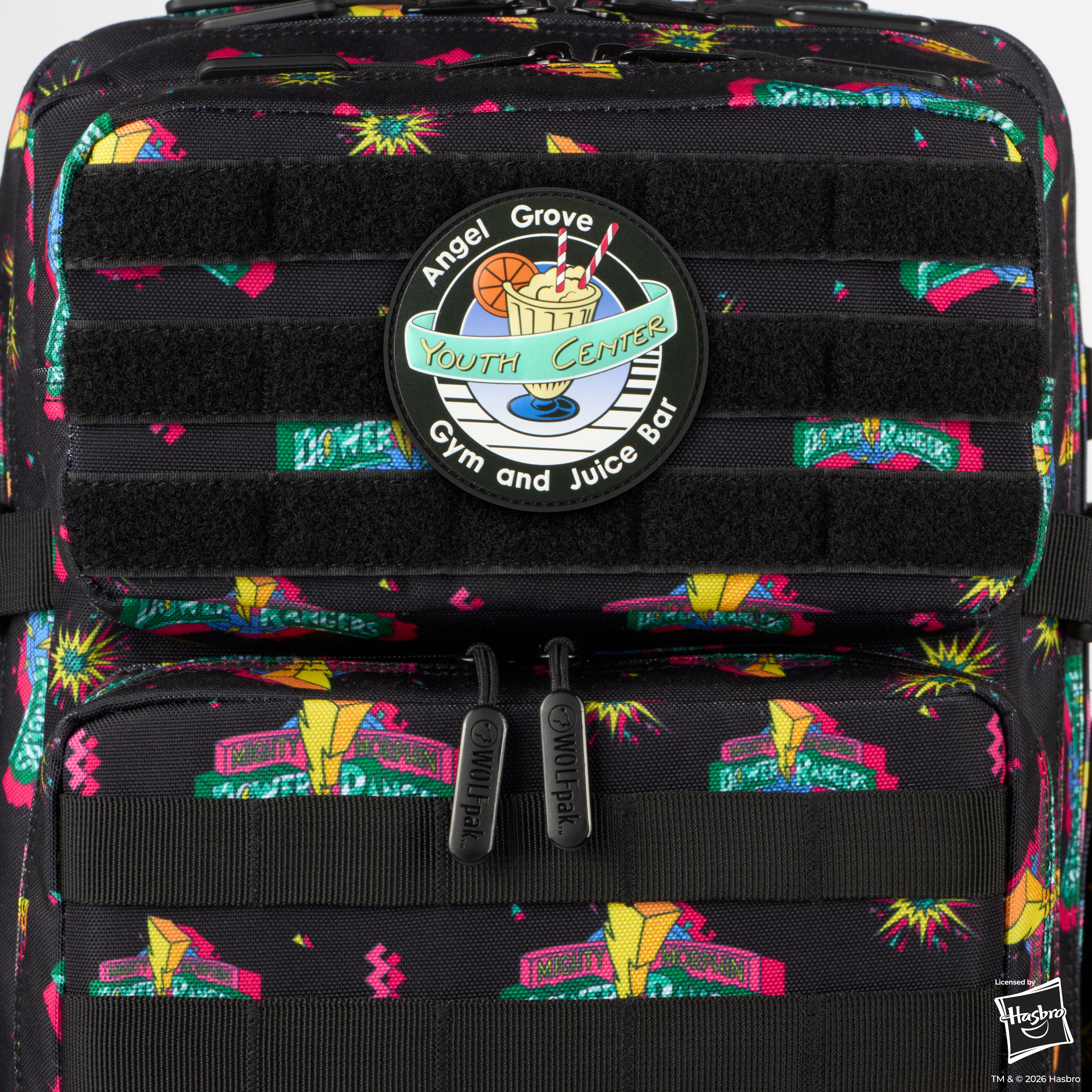 Close-up of a black backpack with a colorful retro-style graffiti pattern and a circular 'Angel Grove Youth Center Gym and Juice Bar' patch on the front pocket.