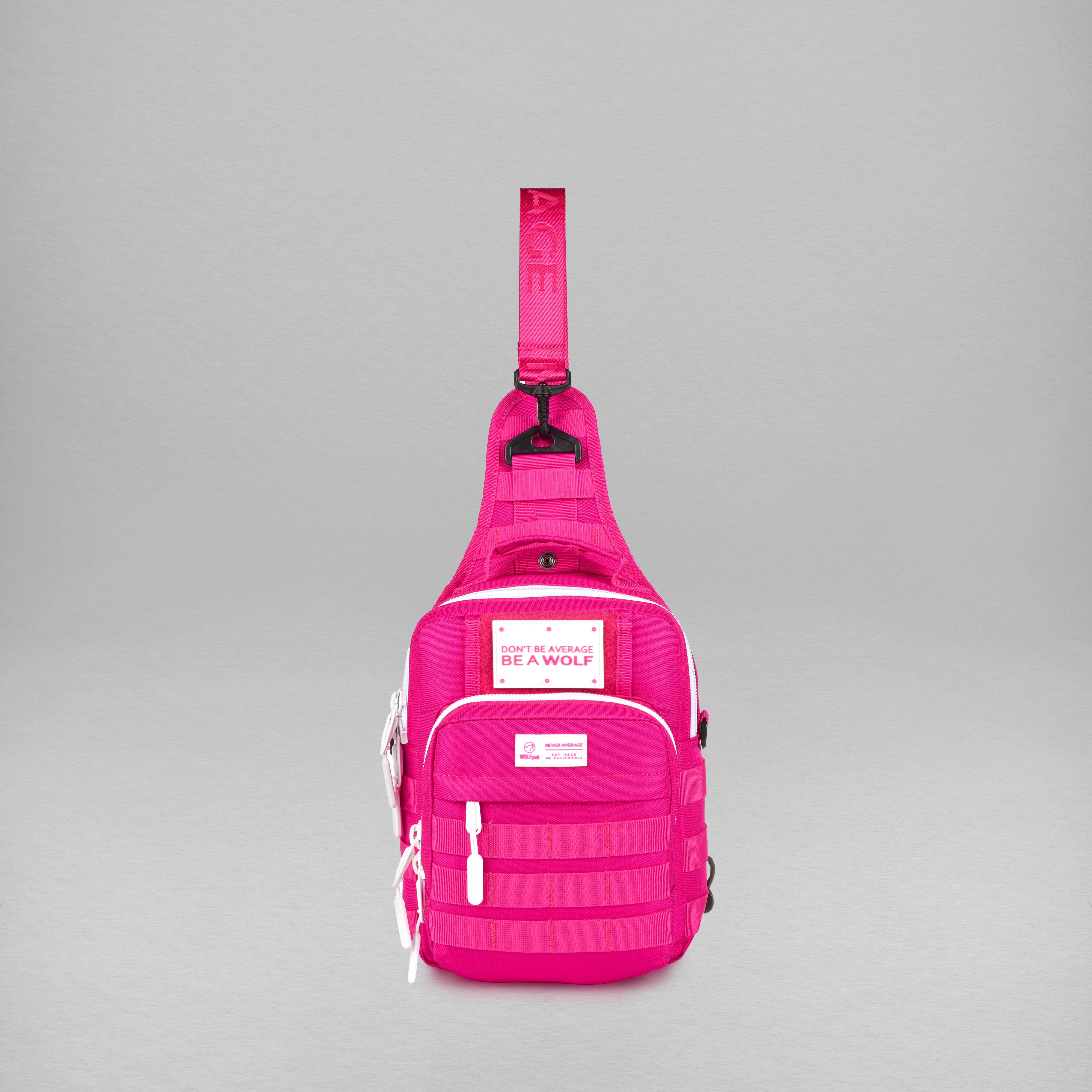 A bright pink tactical sling backpack with multiple zippered pockets and a white 'BE A WOLF' brand patch on the front, photographed against a neutral gray background.