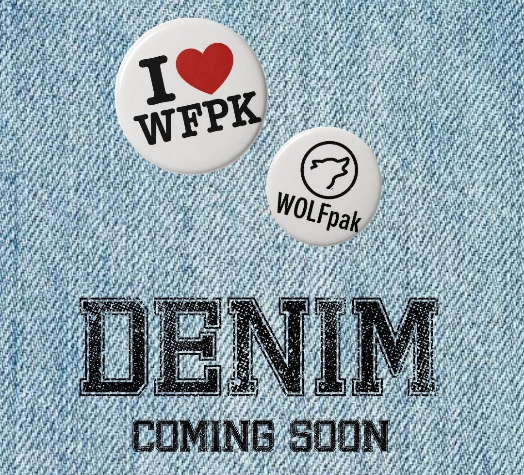 Light blue denim texture background with two small circular pins above the text 'DENIM COMING SOON' in black. One pin reads 'I ❤️ WFPK' and the other reads 'WOLFpak'.